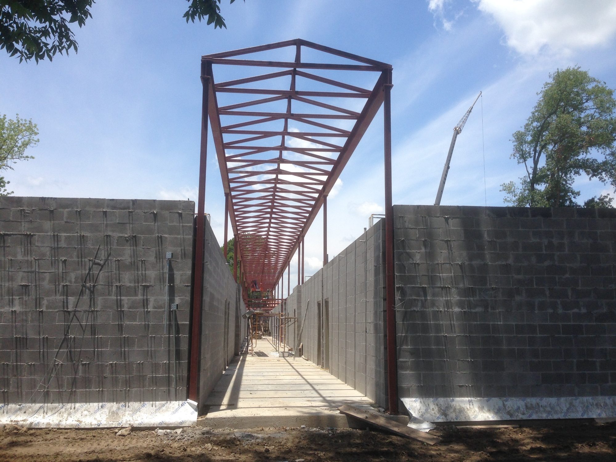 Red steel roof trusses framing corridor between CMU walls